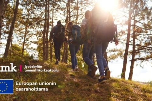 Ryhmä ihmisiä kävelee metsäisessä maastossa ylämäkeen auringon paistaessa taustalta. Kuvan vasemmassa alakulmassa näkyy Jyväskylän ammattikorkeakoulun logo sekä Euroopan unionin lippu ja teksti 'Euroopan unionin osarahoittama'.